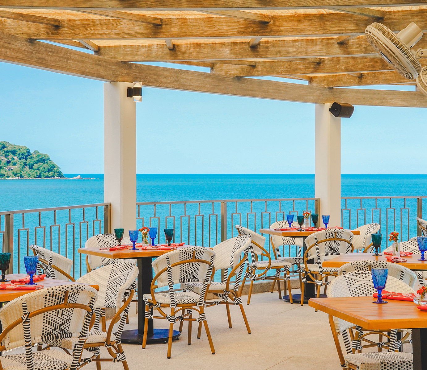 a patio with tables and chairs on a deck overlooking the ocean