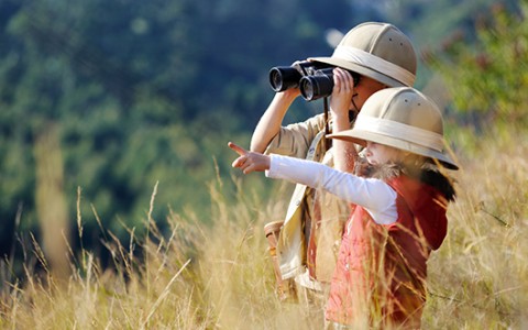 a couple of kids in safari hats looking through binoculars