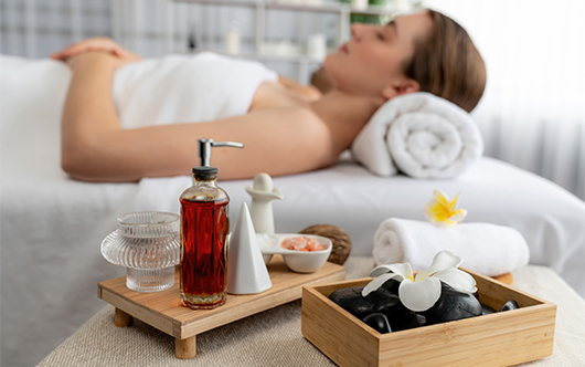 a woman lying on a bed with a bottle of oil and flowers