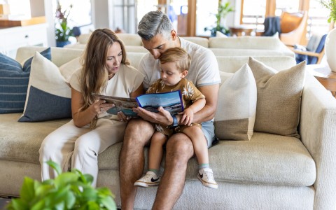 a man and woman reading a book to a child on a couch