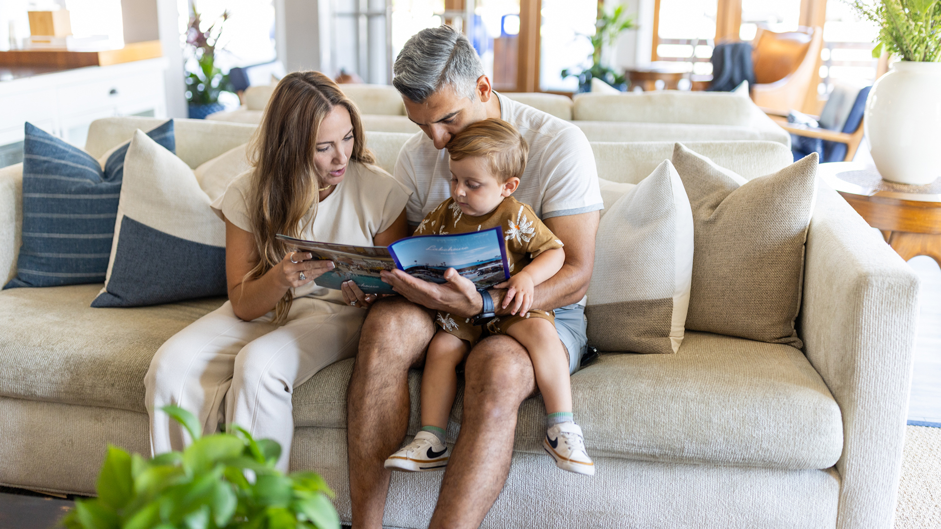a man and woman reading a book to a child on a couch