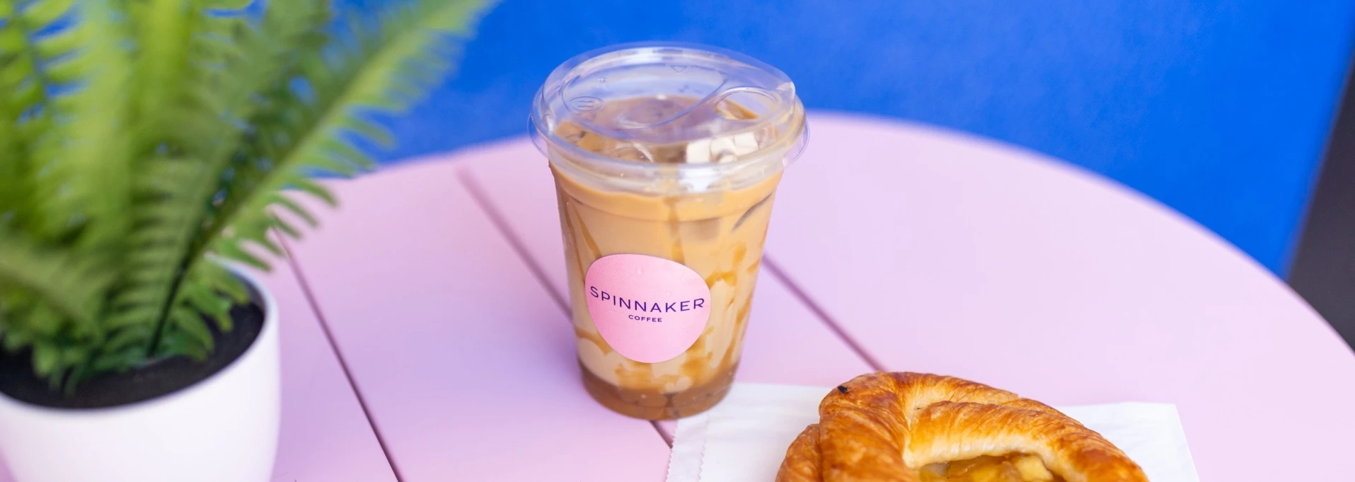 a cup of iced coffee and a croissant on a pink table