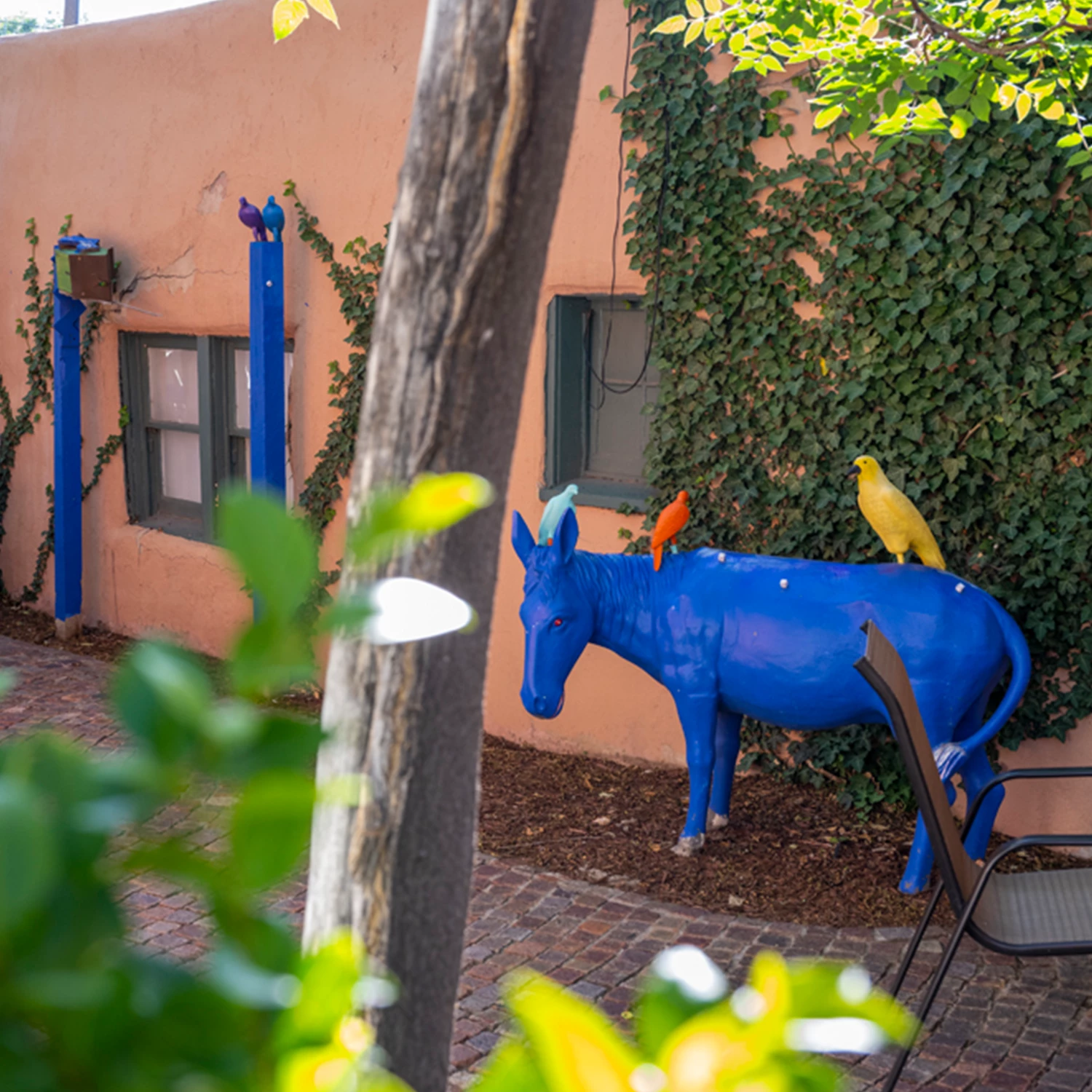 view of a blue donkey with colorful birds in front of a building