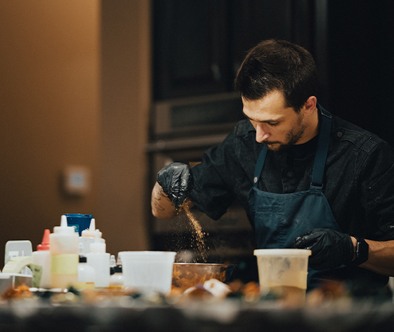 a man in a black apron pouring brown powder into a bowl