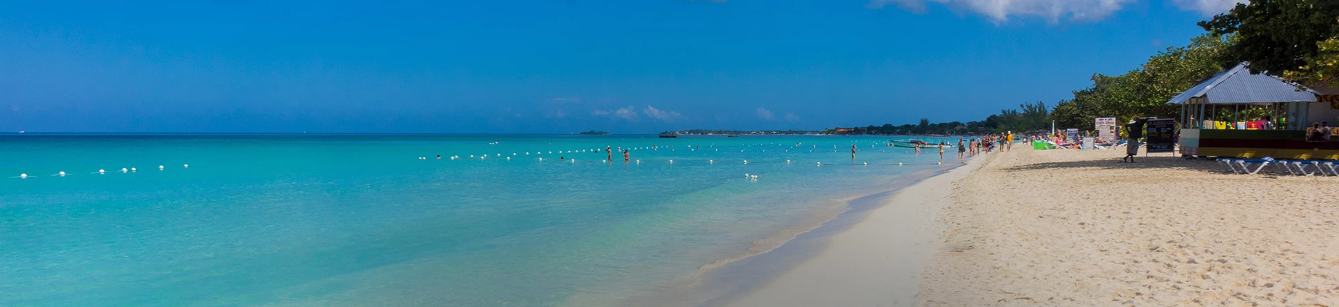 distance shot of sandy white beaches with clear turquoise waters segmented off for swimming and water sports, with people in the distance