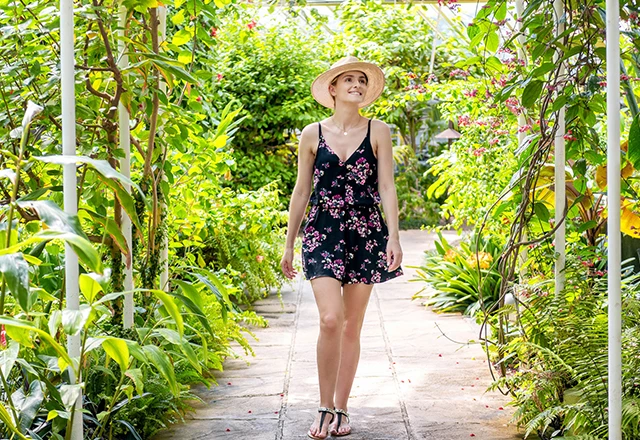 young woman in sundress casually taking a walk along a cobblestone path in a tropical garden