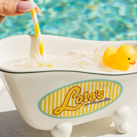 a hand holding a straw in a bath tub with a yellow rubber duck