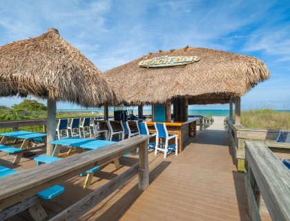 a beach bar with blue chairs and straw roof