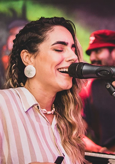 A women in a pink and white stripe shirt on stage singing.