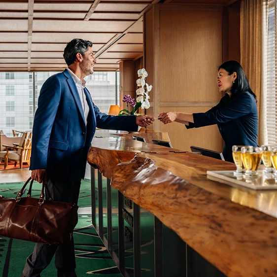 man checking into hotel being greeted and given room key by woman at reception area