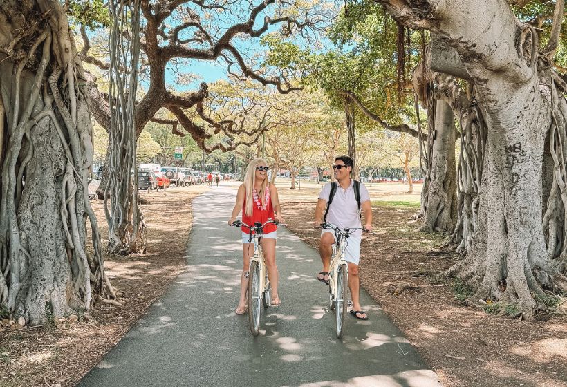 a man and woman riding bikes on a path under trees