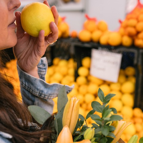 a woman holding a lemon in front of a fruit stand