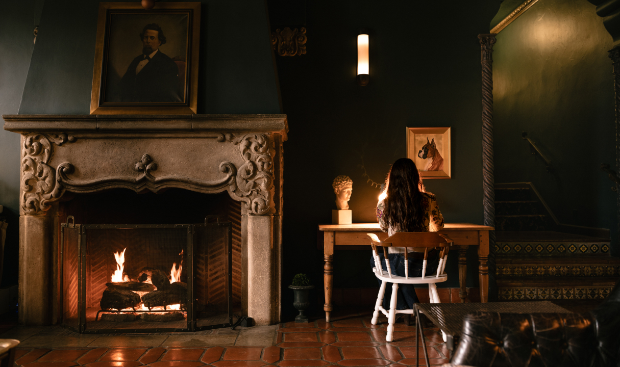 a woman sitting at a table by a fireplace