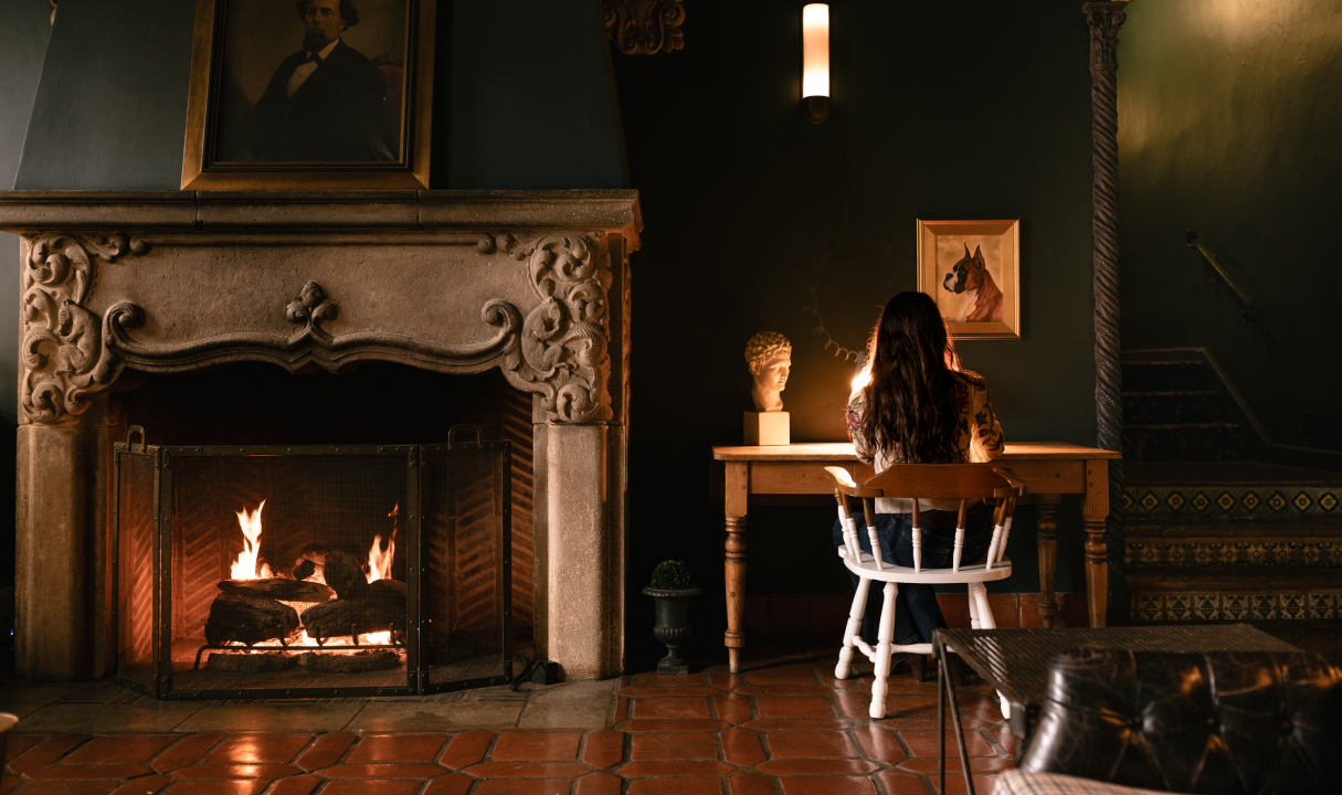 a woman sitting at a table by a fireplace