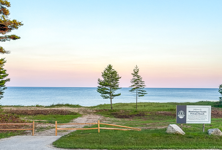 a sign on a grassy area with trees and a body of water
