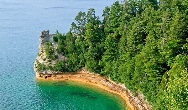 a body of water with trees with Pictured Rocks National Lakeshore in the background
