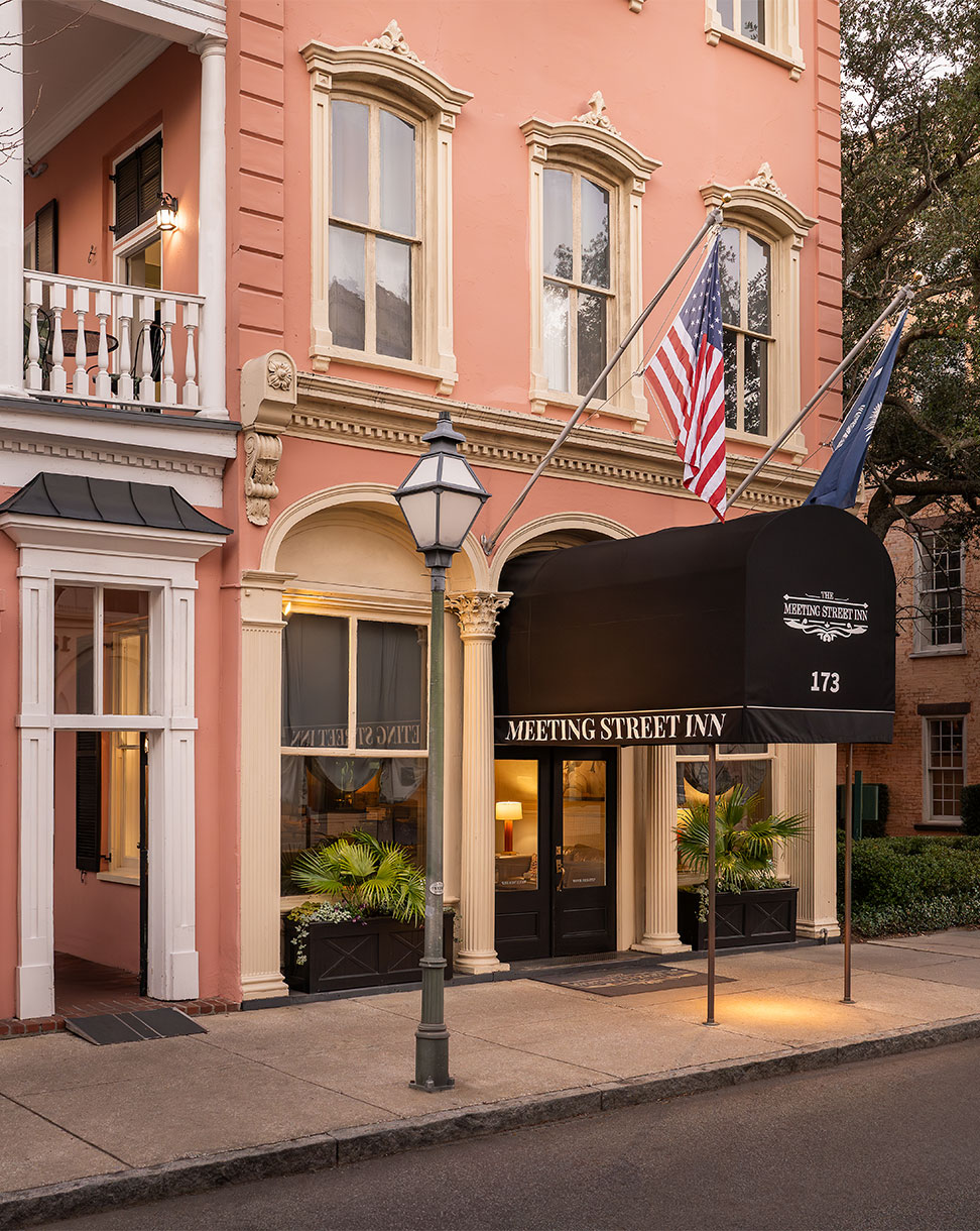A pink building with white trim and a black awning reading 'MEETING STREET INN'