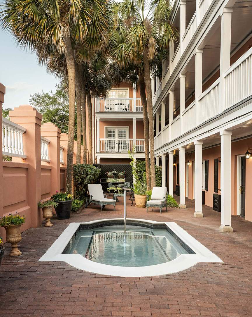 A small pool surrounded by palm trees and seating areas in a courtyard with a building in the background.