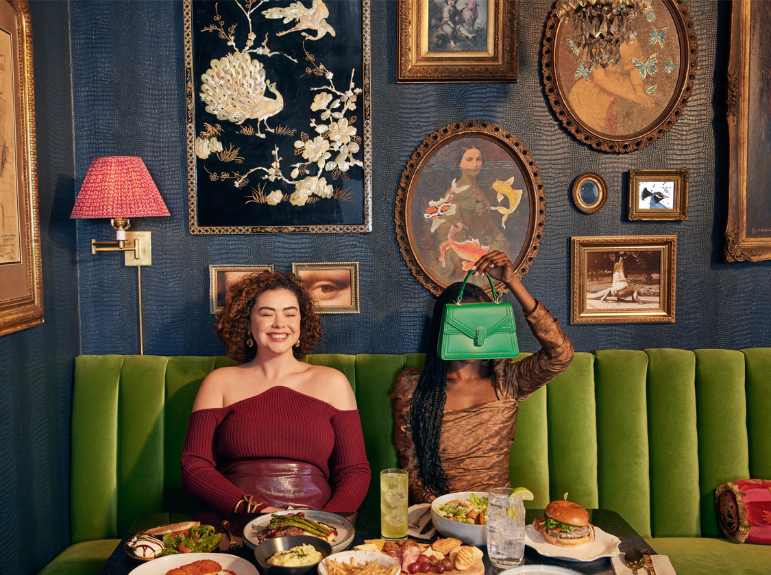 a couple of women sitting on a couch with food and drinks