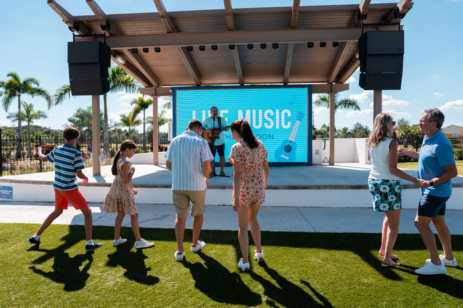 a group of people standing on grass with a man playing a guitar