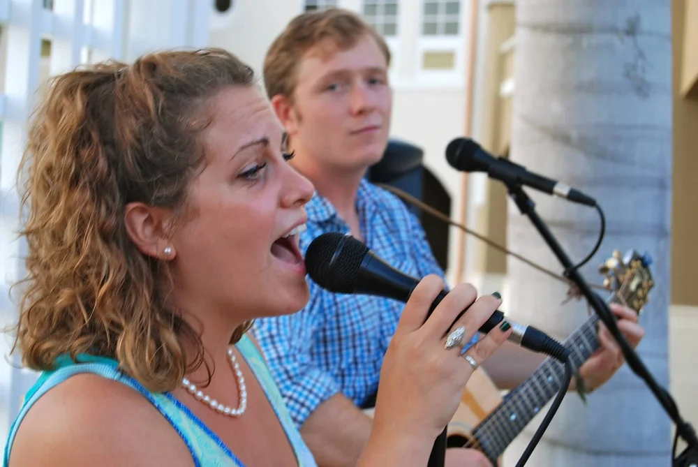 a woman singing into a microphone with a man playing guitar