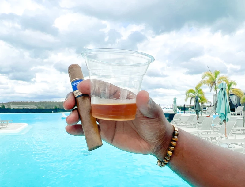 a hand holding a cigar and a glass of liquid