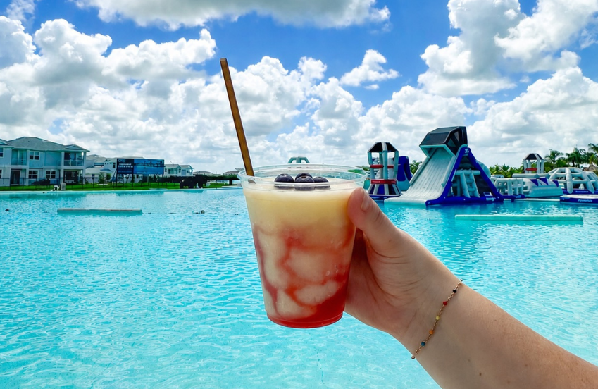 a hand holding a drink with a straw in front of a pool