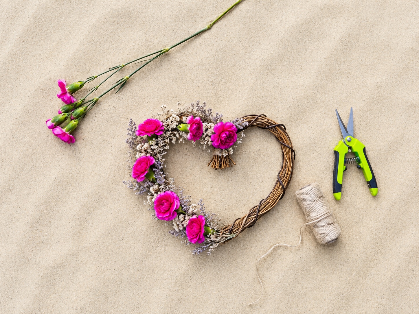 a heart shaped wreath with flowers and scissors on sand
