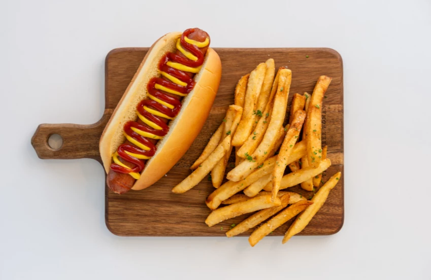 a hot dog with ketchup and mustard on a wooden board