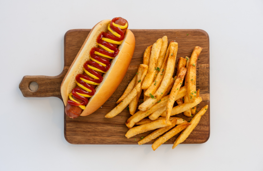 a hot dog with mustard and ketchup on a wooden board