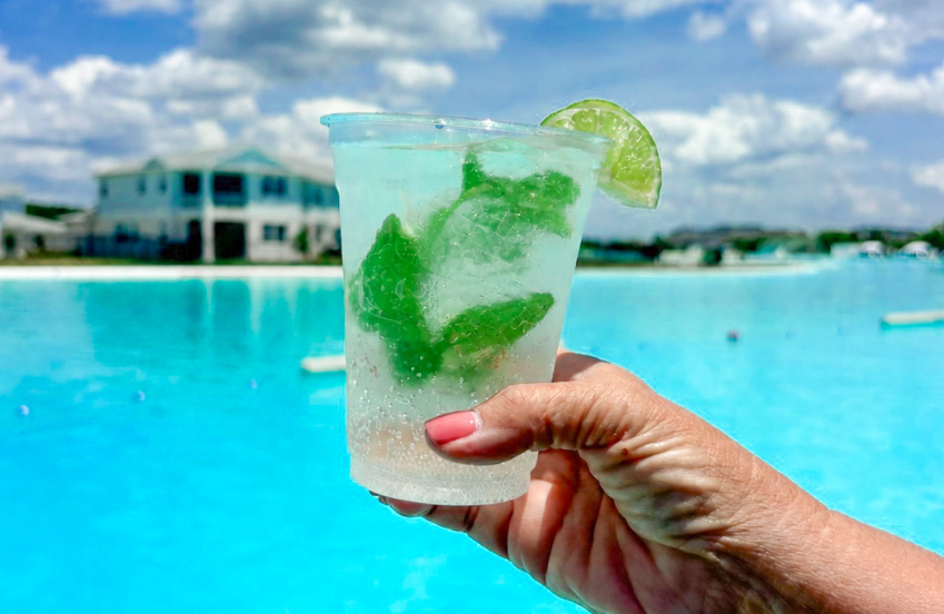 a hand holding a drink with a lime wedge and a pool in the background