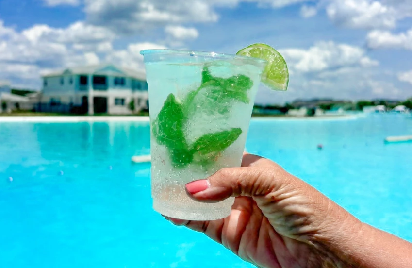 a hand holding a drink with a lime wedge and a pool in the background