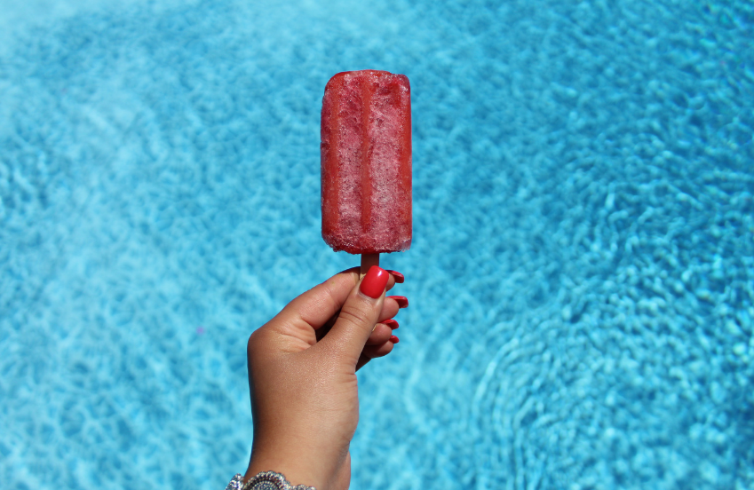 a hand holding a popsicle in front of a pool