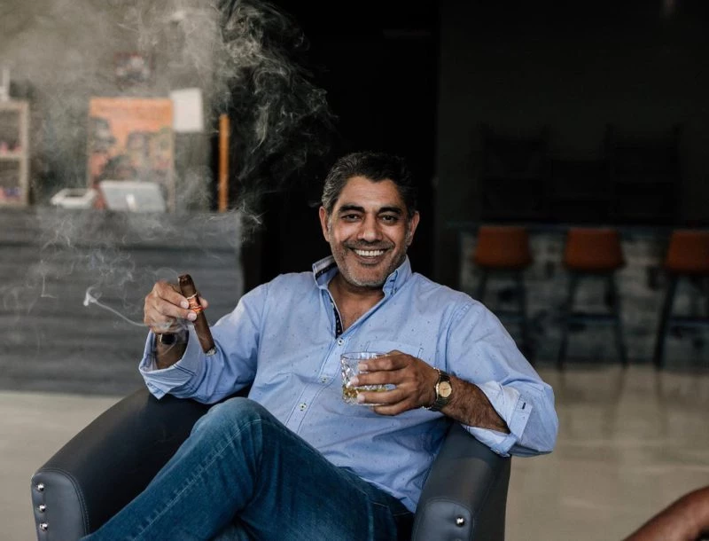 a man sitting in a chair holding a cigar and a glass