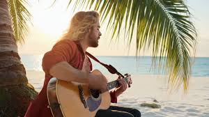 a man playing guitar under a palm tree on a beach