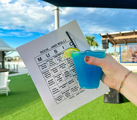 a hand holding a blue drink with a piece of paper and a lime wedge