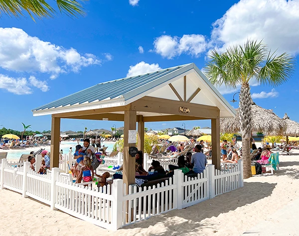 a group of people sitting under a white fence on a beach