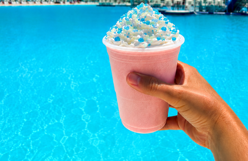 a hand holding a pink drink with whipped cream and sprinkles