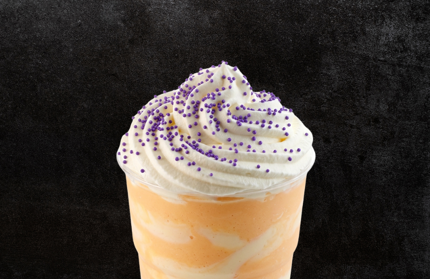 a cup of orange and white liquid with whipped cream and purple sprinkles