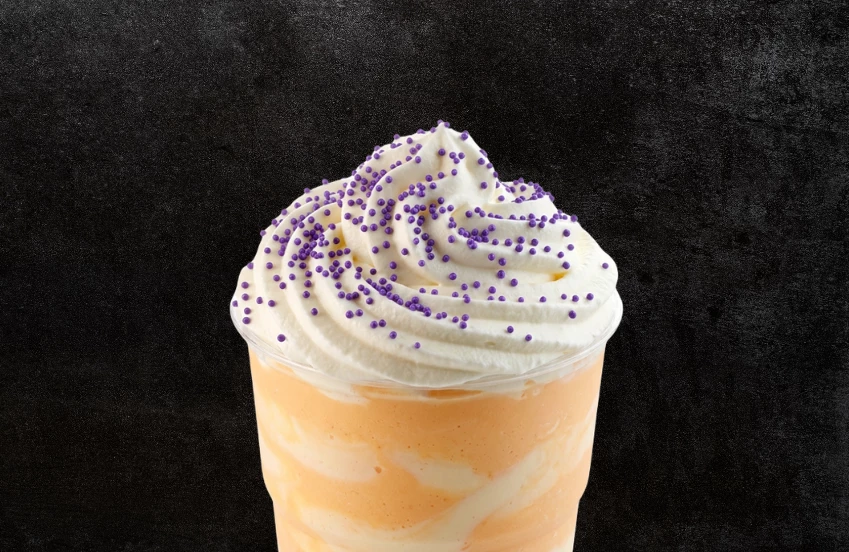 a cup of orange and white liquid with whipped cream and purple sprinkles
