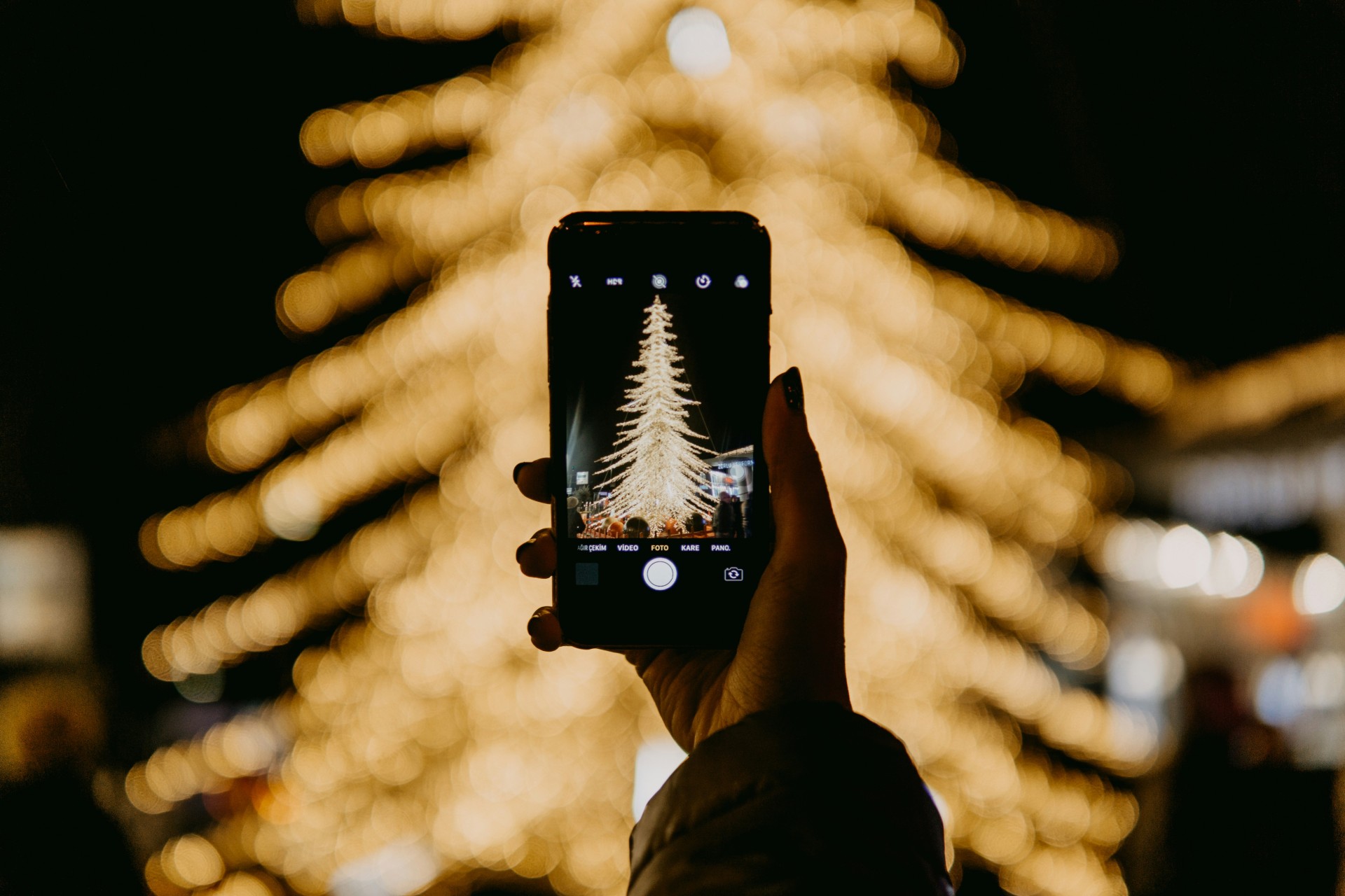 a hand holding a phone with a christmas tree in the background