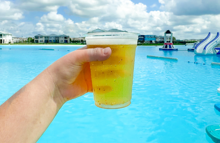 a hand holding a cup of beer by a pool