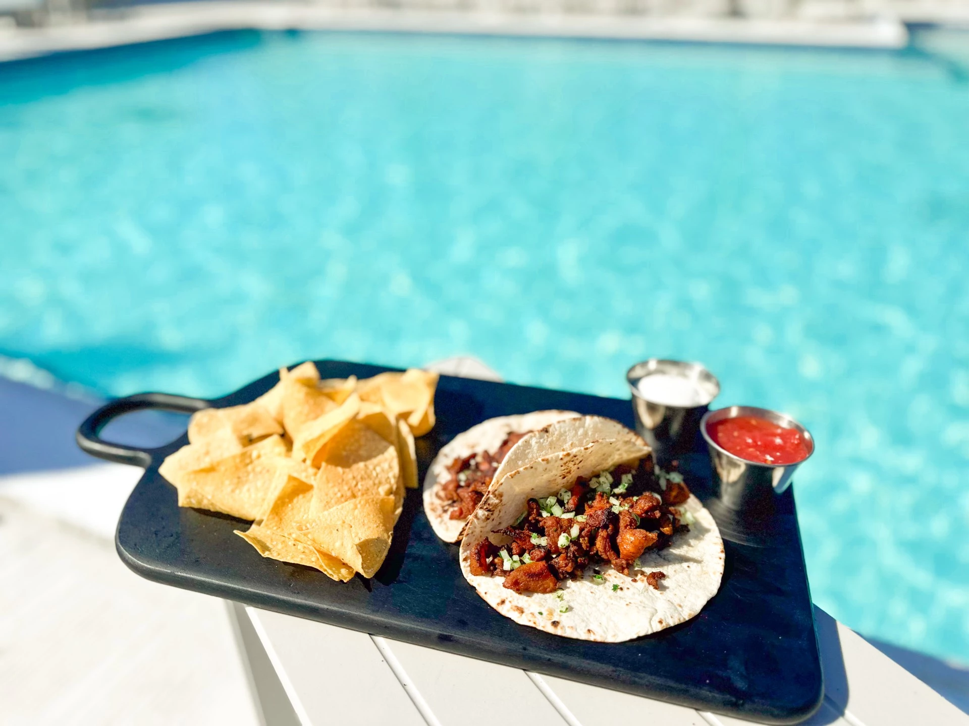 a plate of tacos and chips on a table by a pool
