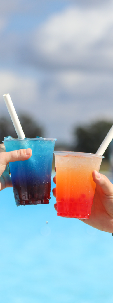 two hands holding drinks with straws