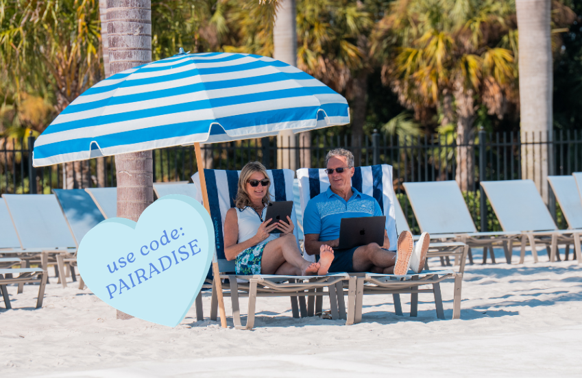 a man and woman sitting on beach chairs under an umbrella