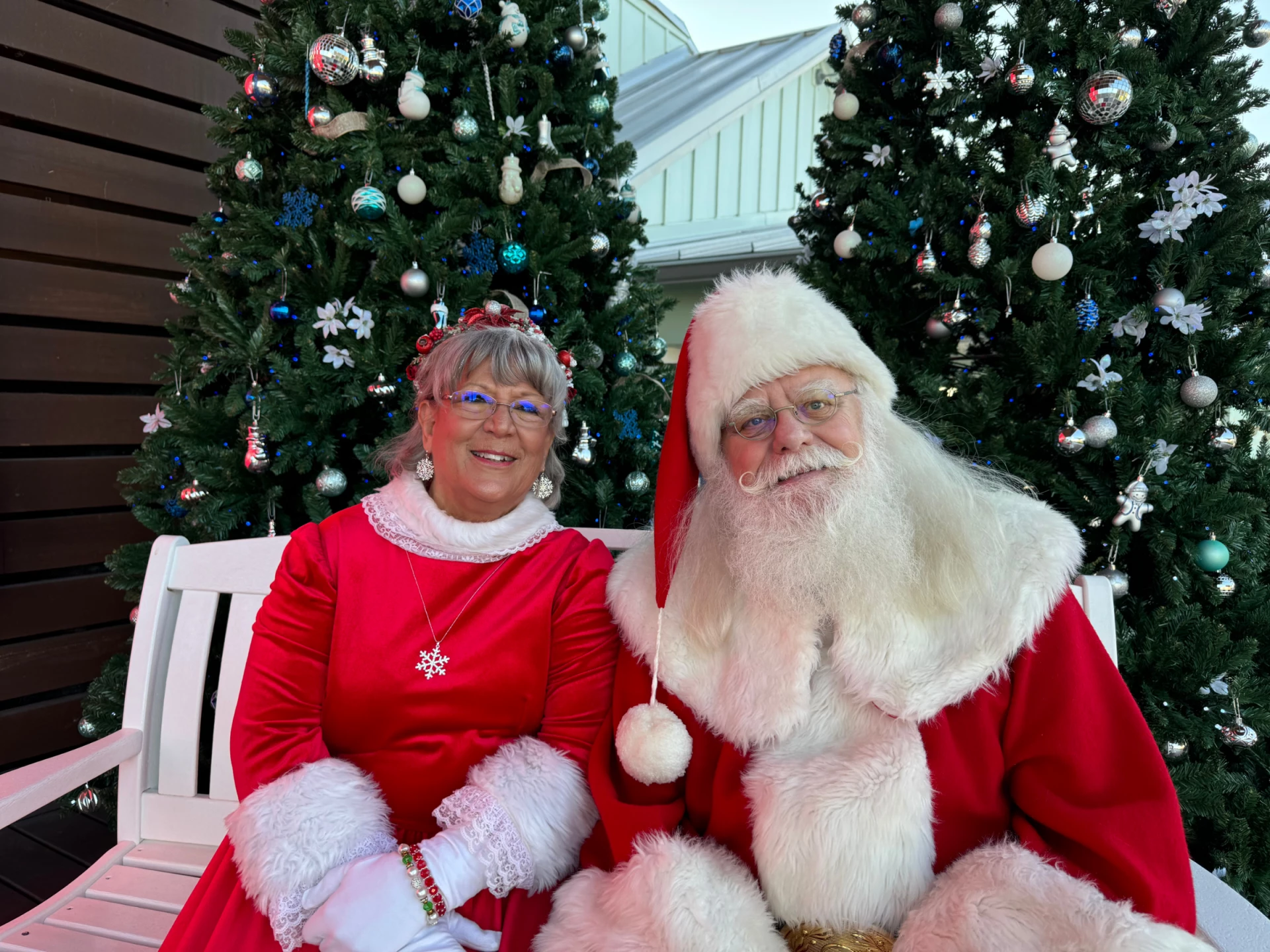 a man and woman in clothing sitting on a bench with christmas trees