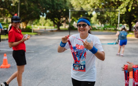 a woman wearing a white shirt and sunglasses holding a red medal