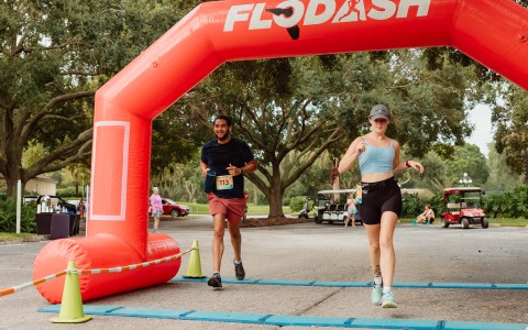 a man and woman running under an inflatable arch