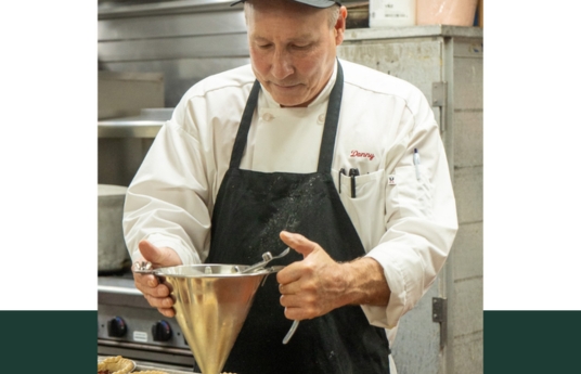 a man in a black hat and apron pouring food into a funnel