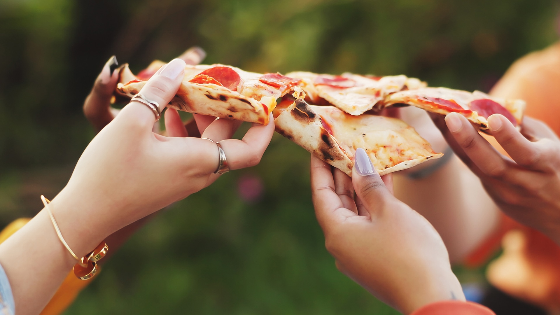 a group of hands holding slices of pizza